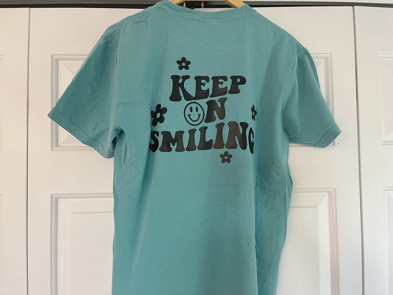 a t - shirt that says keep on smiling hanging on a door