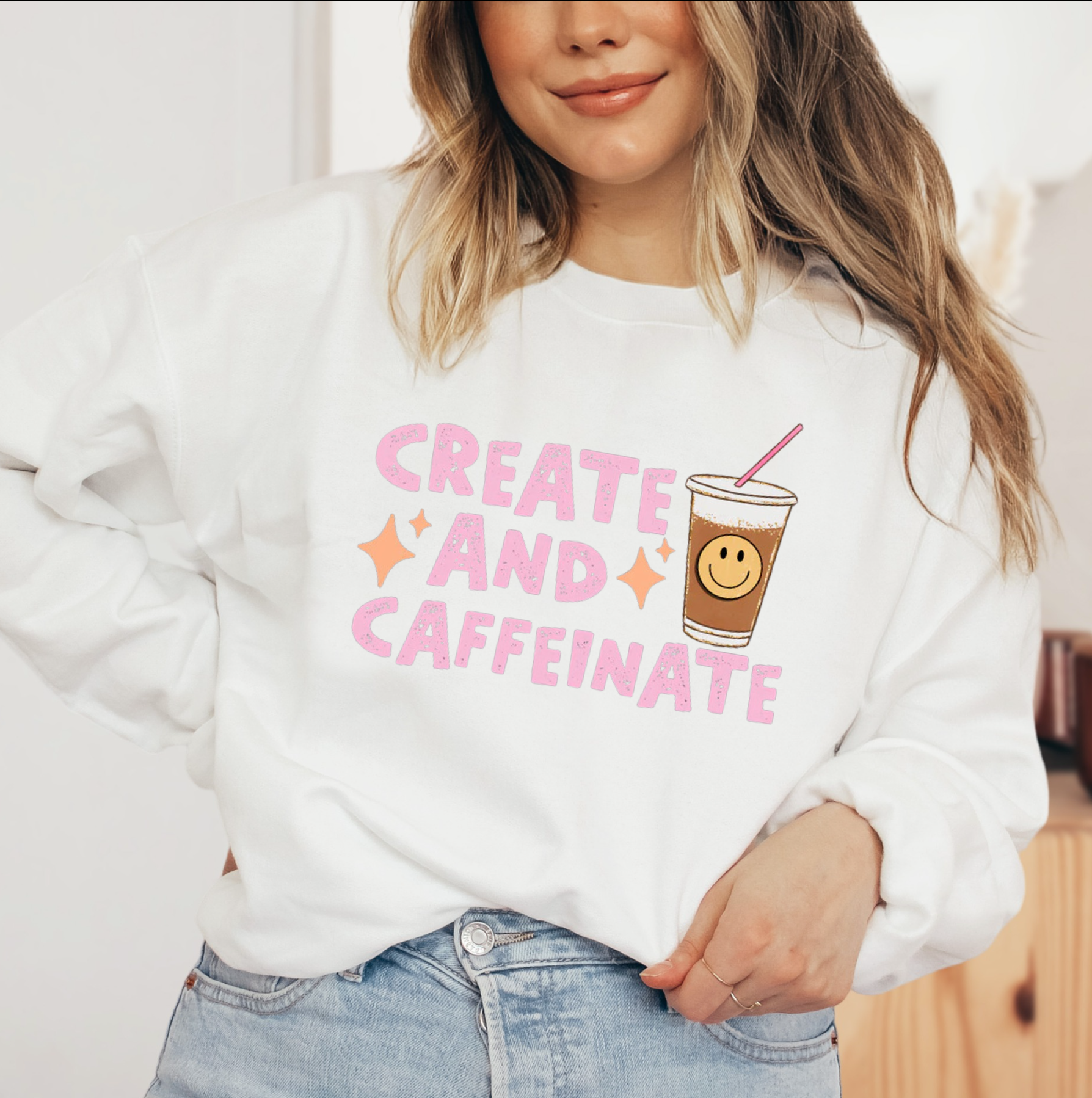 a woman wearing a white sweatshirt that says create and caffeinate