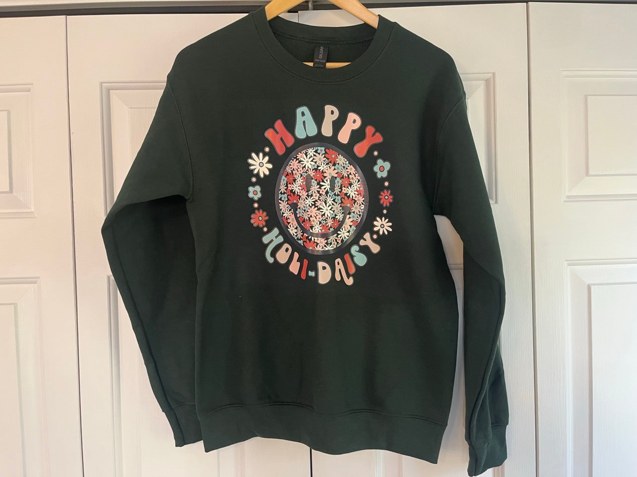 a green happy holidays sweatshirt hanging on a door