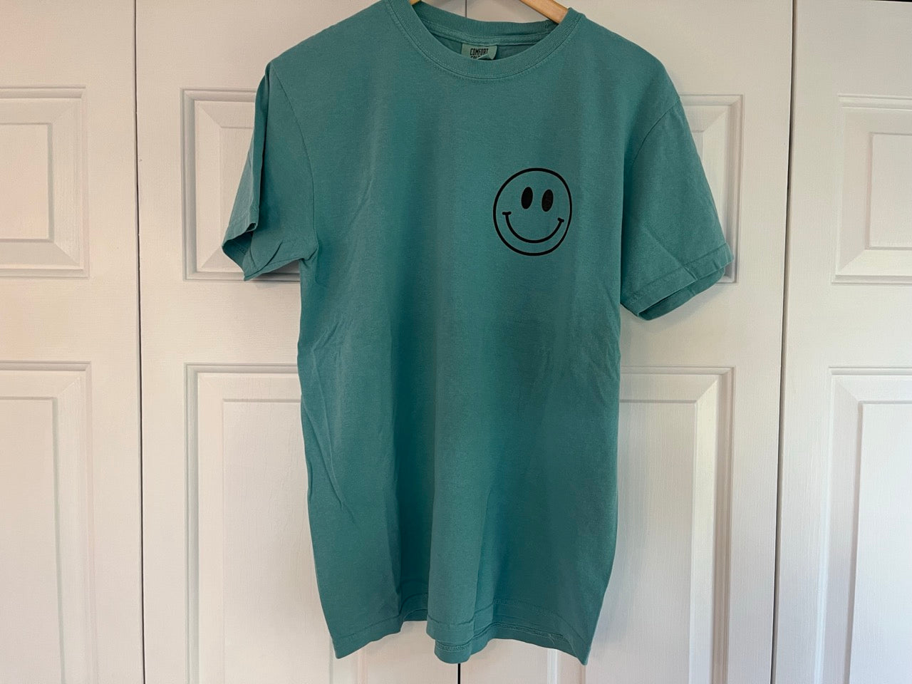 a green t - shirt with a smiley face drawn on it