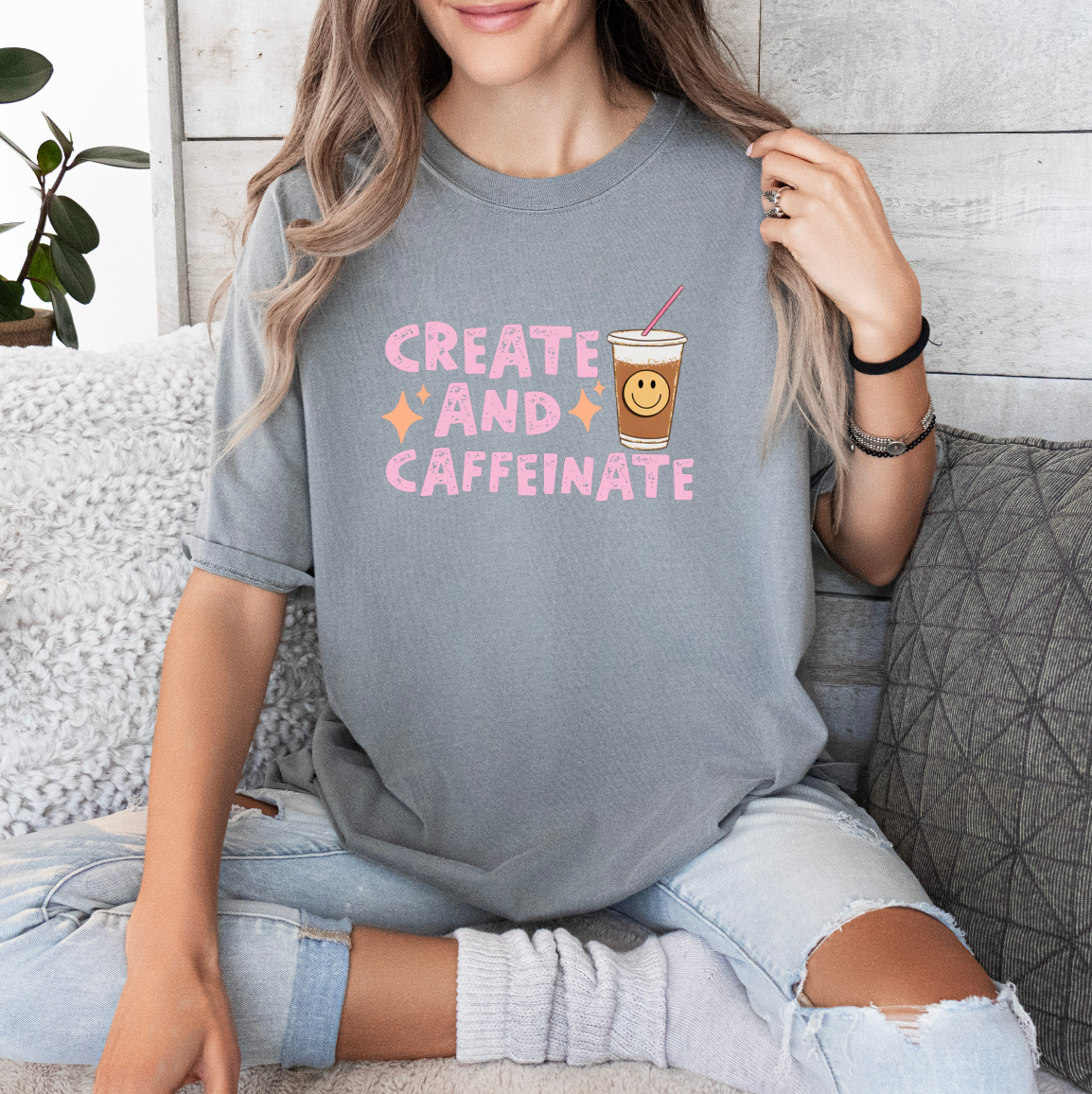 a woman sitting on a couch wearing a grey shirt that says create and caffe